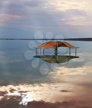 Incredible optical effects at the Dead Sea. The picturesque gazebo for swimmers is reflected in a smooth sea surface.