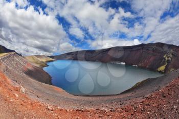 Iceland in July. Oval blue lake in the crater of the volcano cooled down. Steep banks of the lake of red rhyolite