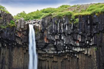 Black basalt faces framed by a jet of water. Magnificent waterfall Svartifoss in Icelandic Skaftafell park