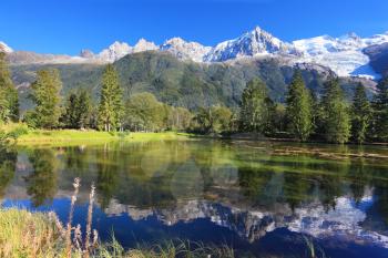 Gorgeous reflection in the smooth water of the lake in the park.  Snowy mountains and evergreen forests in the famous mountain resort of Chamonix 