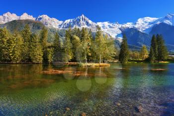 City park in the Alpine resort of Chamonix. Lake with cold water surrounded by trees and snow-capped mountains