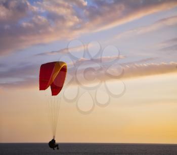 The operated parachute flies low above the sea on a sunset