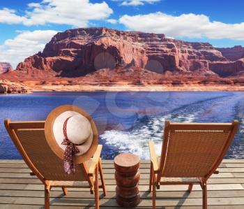 Waves from the boat dissect lakes Powell on the river Colorado. Aft vessels cost two chaise lounges. On a back of one the elegant straw women's hat hangs