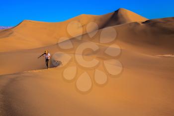 Sunrise in the orange sands of the desert Mesquite Flat, USA. Woman - photographer is among the gently sloping sand dunes