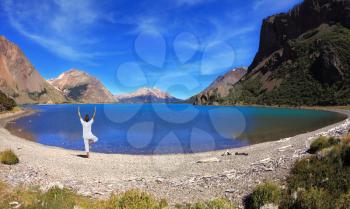 Yoga on the lake. Mature woman in white performs asana tree, standing on the shore of round lake