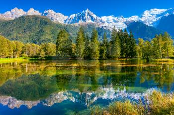 Early fall in Shamoni,  France. The snow-covered Alps and evergreen fir-trees are reflected in lake