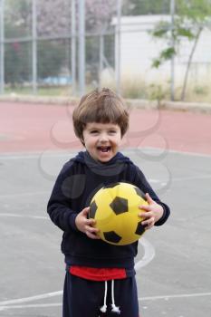 A lovely little boy played happily with a yellow ball on the playground
