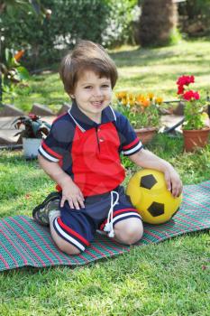 A little boy with a charming smile, poses on a green lawn. He carried a yellow ball

