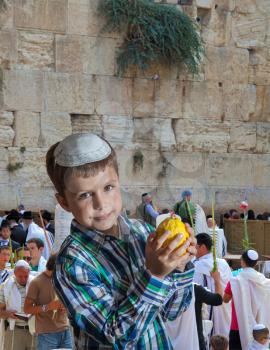 Sukkot at the Western Wall of Temple in Jerusalem. Charming seven year old boy in white festive skullcap with etrog