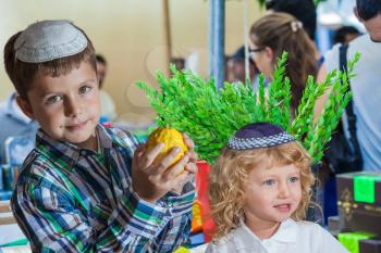 The Jewish holiday of Sukkot,  Holiday market in Jerusalem. Cute little boy with long blond hair in  knitted skullcap and  seven year old boy in white skullcap with etrog. Ritual plants - myrtle prepa