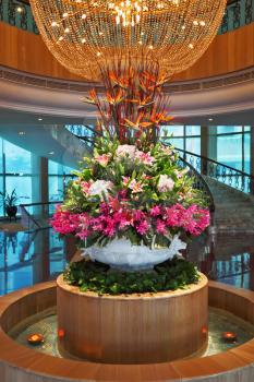 The huge magnificent crystal chandelier and flower bed - a vase decorate a hall of expensive hotel
