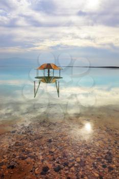 Medical beach on the Dead Sea, Israel. Round gazebo in the water near the water's edge. Cloudy sky reflected in water