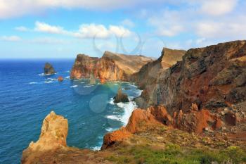 Eastern tip of the island of Madeira. Red and orange rocks cool grow out of foamy waves of the Atlantic Ocean