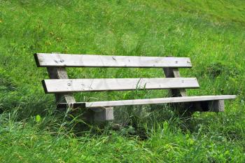 On a hillside in the high grass is a cozy bench