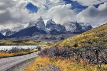 Windy day in the Chilean Patagonia. Picturesque clouds are flying in the blue sky. Gravel road near the lake goes to the famous cliffs of Los Kuernos