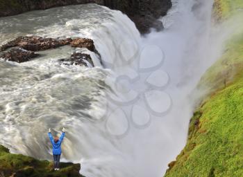 The delighted woman - tourist over  water chasm. Enormous falls Gyullfoss. Summer in Iceland