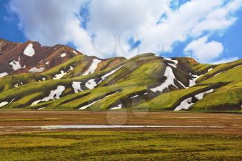 Magnificent colorful mountains. Reserve Landmannalaugar, Iceland. Green moss on smooth slopes and white spots snowfields in the gullies