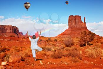 Navajo Reservation in the US. Woman in white doing yoga. Fly over the valley huge balloons