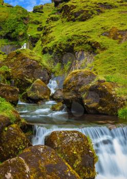 Iceland. Gorgeous cascading waterfall from melting glacier. Basalt mountains covered in green grass and moss