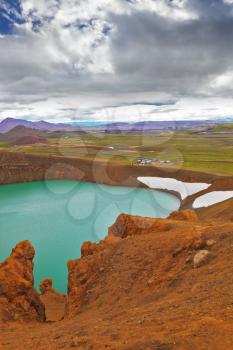 Picturesque lake in the crater of an extinct volcano. Lake water bright green color. On the shores lie snowfields from last year. Summer in Iceland