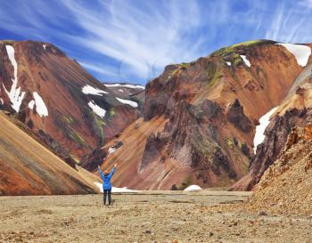 Smooth orange rhyolite mountains in Landmannalaugar nature reserve. The woman - tourist in blue jacket, raised her hands in delight