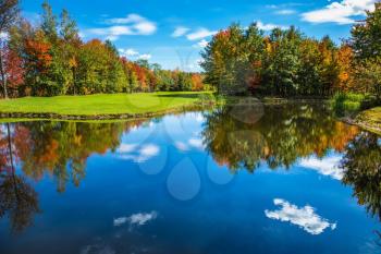Golf Club on the road to Bromont, French Canada.  Park of fantastic beauty. Concept of Golf tourism. Red, orange and green autumn foliage is reflected to clear water of the lake