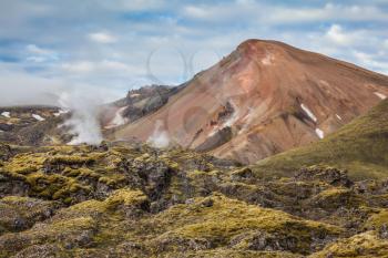 Picturesque rhyolite mountains surround the valley. In the hollows of the mountains from the ground rises 
steam.  Summer morning in the National Park Landmannalaugar, Iceland