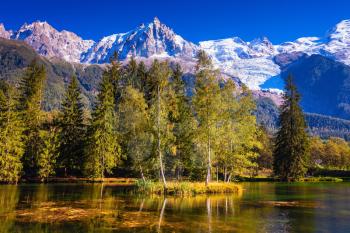 Early fall in Shamoni, Haute-Savoie. France. The snow-covered Alps and evergreen fir-trees are reflected in lake