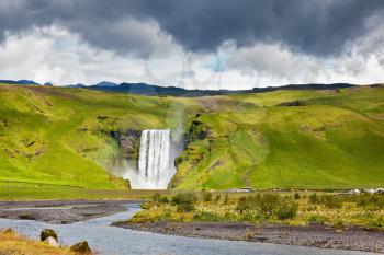 Huge picturesque waterfall and creek running along the road. Iceland, waterfall Skogafoll