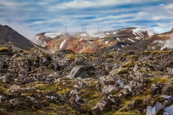 In the hollows of the mountains from the ground rises steam. Rhyolite mountains surround the valley.  Summer morning in the National Park Landmannalaugar, Iceland