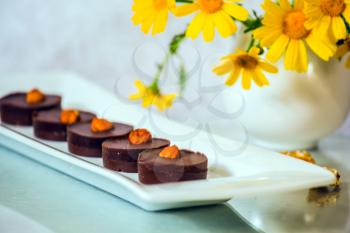 Gorgeous confectionery desserts. Portion chocolate cakes are decorated with nuts. Background - a white vase with field chamomiles. Professional bakery
