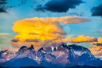 Snow-covered rocks and cumulus clouds in the orange sunset. The black cliffs of Los Cuernos. The concept of extreme and active tourism. Torres del Paine National Park