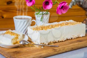 Delightful cheesecake with crumbled kadaif. Professional bakery. On a saucer with a spoon lies a piece of cake. The background is cup with tea and vase with flowers