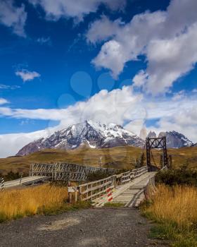 The famous Torres rocks. Wooden narrow bridge through a small stream. Mountains  in Torres del Paine National Park, Chile. The concept of active and extreme tourism