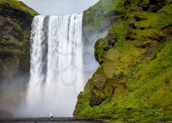 Grand waterfall Skogafoss in Iceland. Tourist in shirt and bandana threw up his hands with delight the beauty of nature