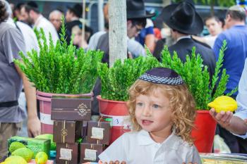The Jewish holiday of Sukkot. Cute little boy with long blond hair in  knitted skullcap. He stands on a pre-holiday market in Jerusalem