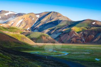 Snow lies in the hollows of colorful rhyolite mountains. Green Valley is flooded with melt water.  Early summer morning in the National Park Landmannalaugar, Iceland