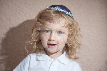 The charming little boy with blue eyes and long blond curls in Jewish knitted skullcap. Autumn holiday of Sukkot