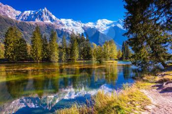  The snow-covered Alps and evergreen fir-trees  reflected in lake. Early fall in Chamonix, Haute-Savoie