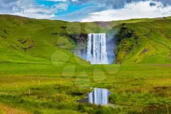 Grandiose reflection. The huge deep falls Skogafoss are reflected in small stream