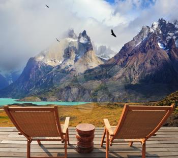 Pleasant holiday in Chile. Wooden chairs in the park Torres del Paine. On the horizon is visible snow-covered rocky mountain