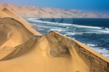 The concept of extreme and exotic tourism. Ocean surf with foamy waves. Jeep - safari through the huge sand dunes on the ocean shore. Atlantic coast of Walvis Bay, Namibia, south of Africa