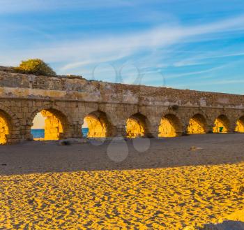 Ruins of the high aqueduct of the reign of Herod the Great. The sandy beach is trampled by tourists. Concept of active and historical tourism