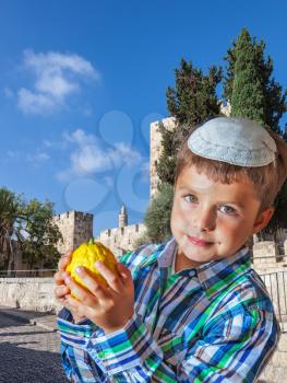 Jerusalem, Israel. Autumn Jewish holiday Sukkot. Beautiful Jewish boy with green eyes, in a white skullcap, with citrus in his hand
