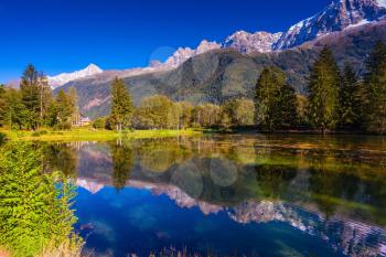  The snow-covered Alps and evergreen fir-trees are reflected in lake. Early fall in Chamonix, Haute-Savoie. France