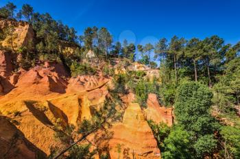  Multi-colored ocher outcrops - from yellow to orange-red. Green trees create contrast with the ocher. Roussillon, Provence Red Village