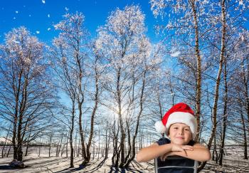 Christmas in the Arctic. Very handsome boy in a red Santa Claus hat on the edge of a winter forest.   Sunny and snowy winter day. Concept of the children's tourism