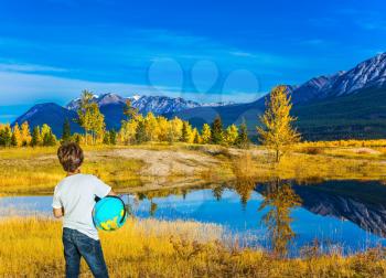 Exquisite Abraham Lake with turquoise water in Canada. Boy in jeans with a globe in his hands admires the lake. Indian Summer in the Rockies. Concept of ecological and active tourism