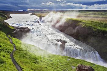 Iceland. Grand Gullfoss. In mid-July, bubbling water illuminated by a bright morning sun