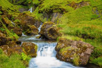 Iceland. Gorgeous cascading waterfall from melting glacier. Basalt mountains covered in green grass and moss